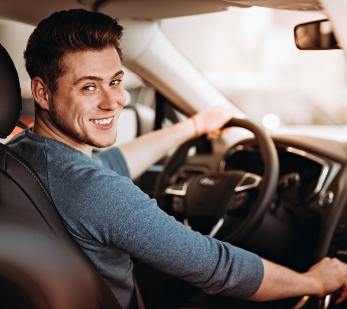 Man smiles over his shoulder in drivers seat of car